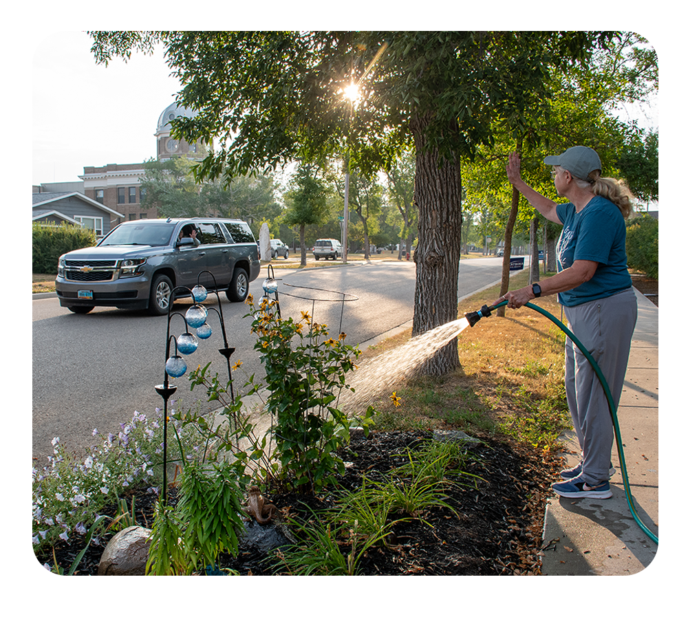 Woman watering her flowers and waiving to a passing vehicle